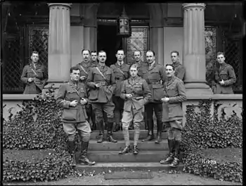 Several men dressed as military officers standing on the verandah of a stone building