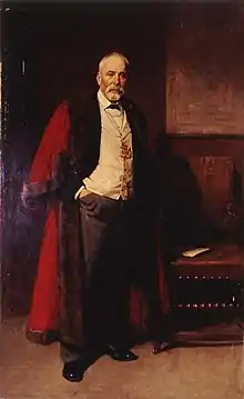 James Walker standing upright, one hand in pocket, wearing fur-trimmed red robe