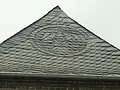 Slate roofers guild emblem as an ornament made with slate roof shingles, Meerbusch, Germany. Note the hip shingles act as a ridge cap.