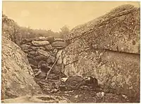 Black and white photograph of a dead soldier, lying on his back, facing slightly towards the lens, amidst rocks.