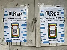 Photograph of two white signs with mostly black text and colorful artwork, taped to a surface