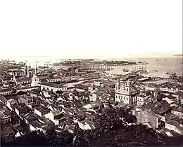 Photographic aerial view of the city from a hillside with ships at anchor in the harbor and island in the background