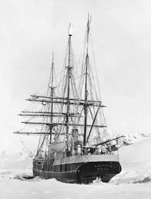 Rear view of a three-masted sailing ship with all sails furled, lying in an ice-covered sea.